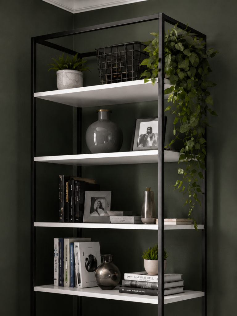 Modern black metal bookshelf styled with green trailing plants, ceramic vases, and books against a dark green wall.